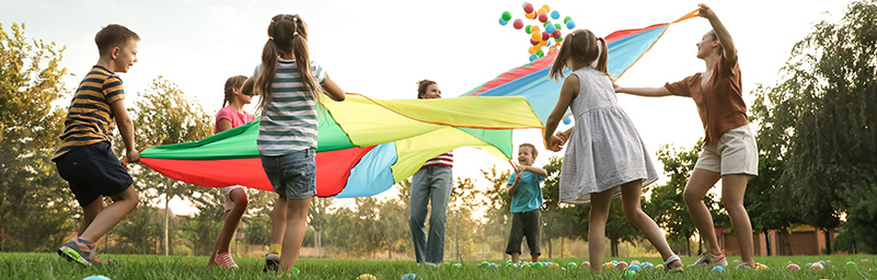 A group of children playing a game outside with a rainbow parachute and coloured balls
