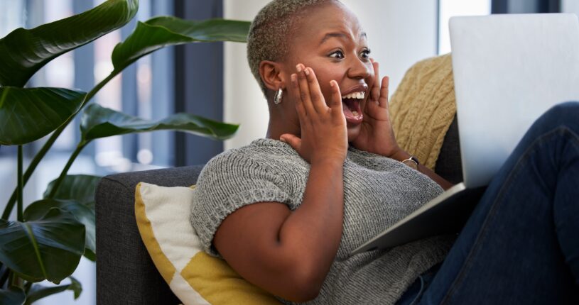 Laptop, surprise and excited woman on sofa shocked with win of digital lottery, competition or award. Wow news, prize winner and girl on gambling website play online poker, bingo or casino game.