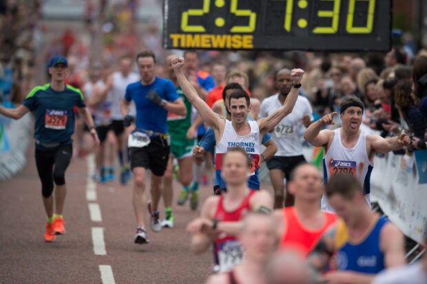 Runners at the Manchester Marathon running along the road being cheered by spectators.