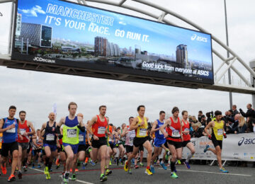 Runners at the Manchester Marathon running along the road being cheered by spectators.