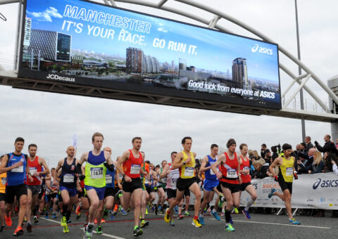 Runners at the Manchester Marathon running along the road being cheered by spectators.